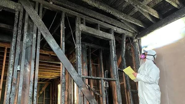 A technician assessing burned wall framing before reconstruction begins
