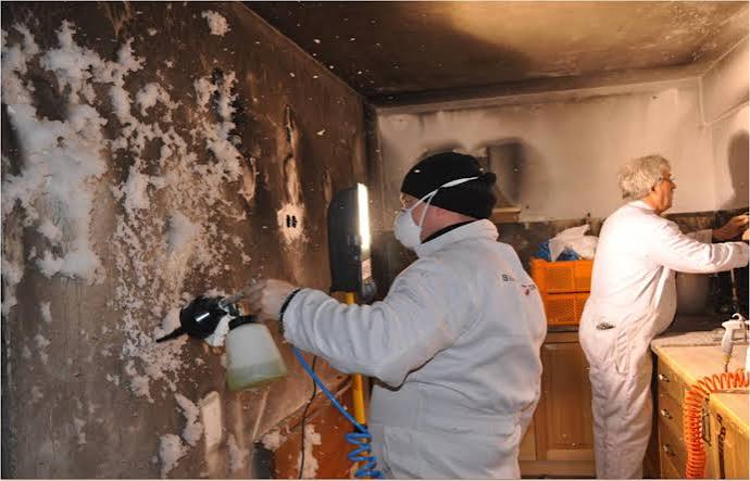 A technician cleaning soot residue off a fire-damaged wall